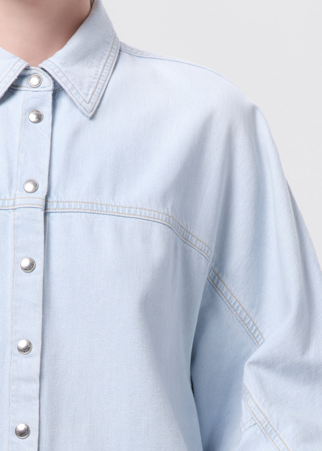 Light blue denim shirt with button details on a neutral background