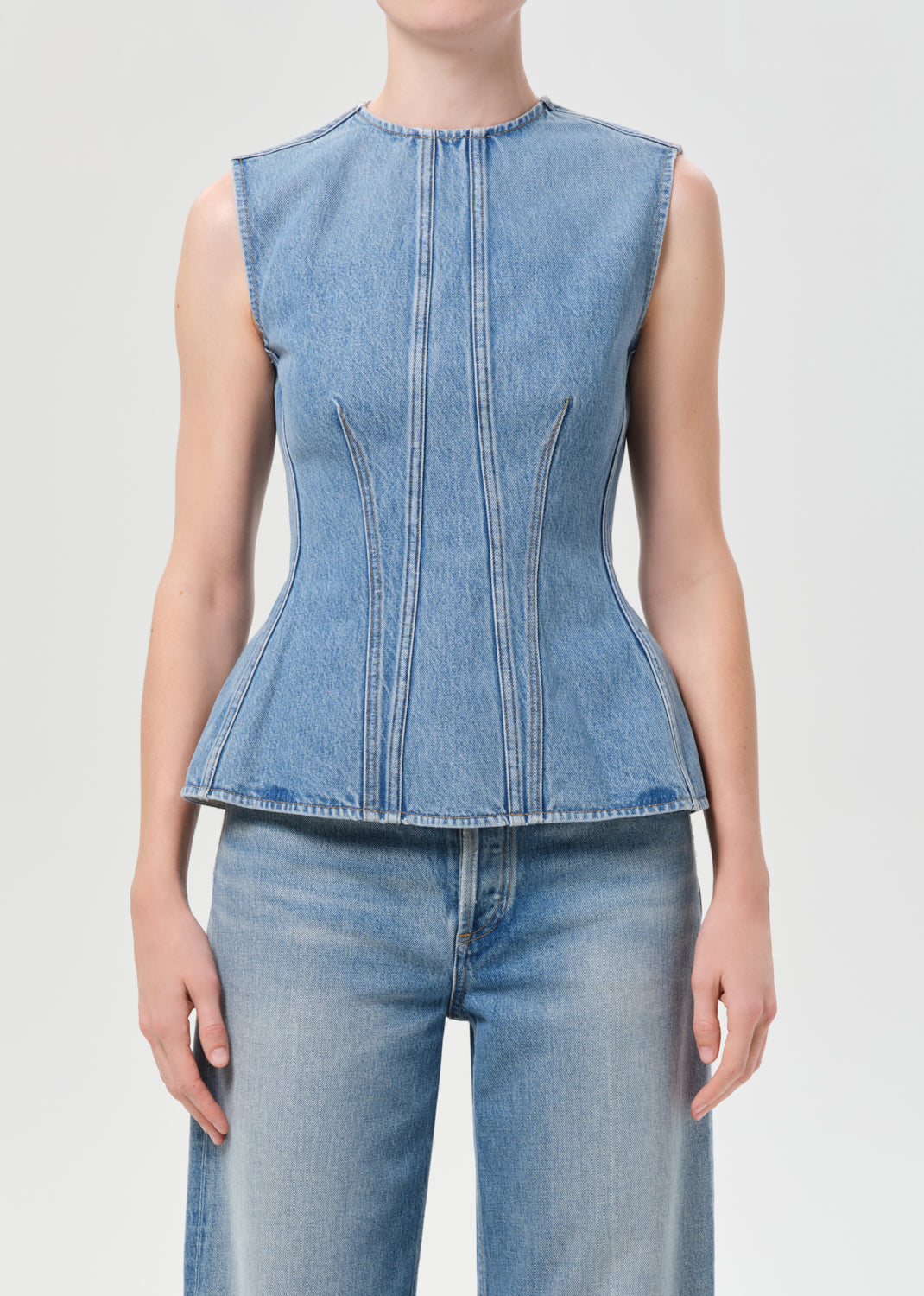 Person wearing a sleeveless denim top and jeans on a plain background