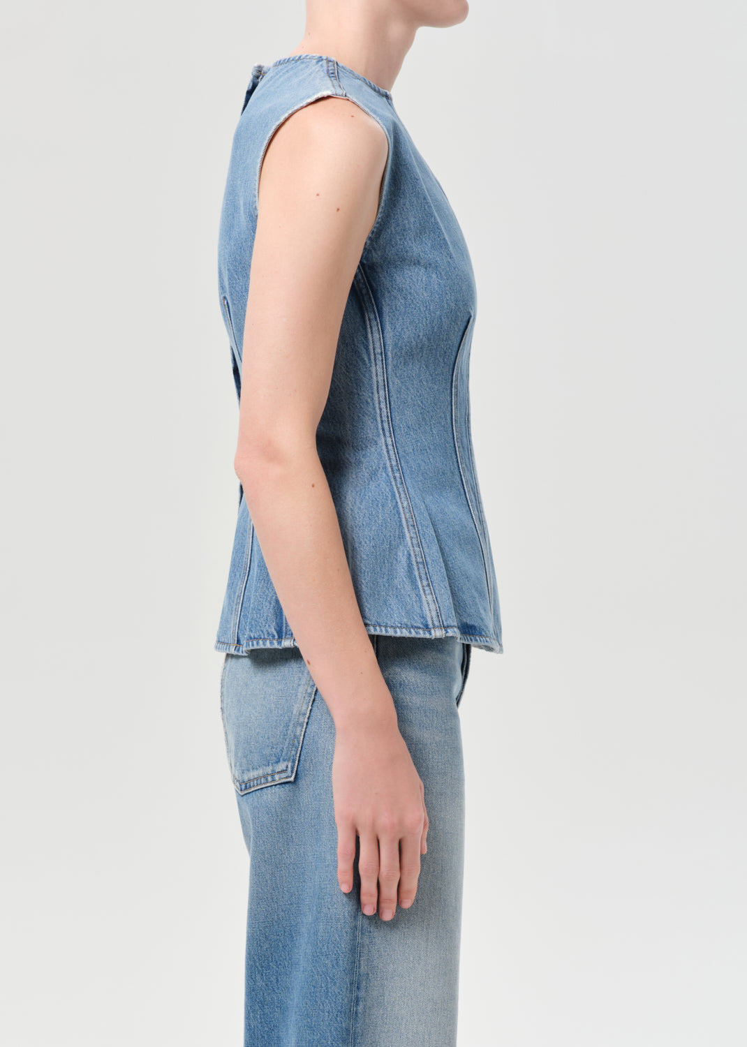 Person wearing a sleeveless denim top and jeans on a light gray background