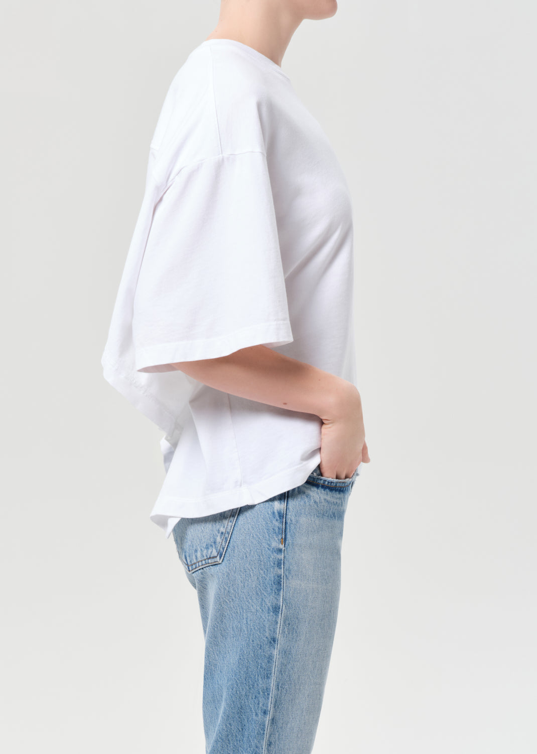 Person wearing a white oversized t-shirt and light blue jeans on a plain background