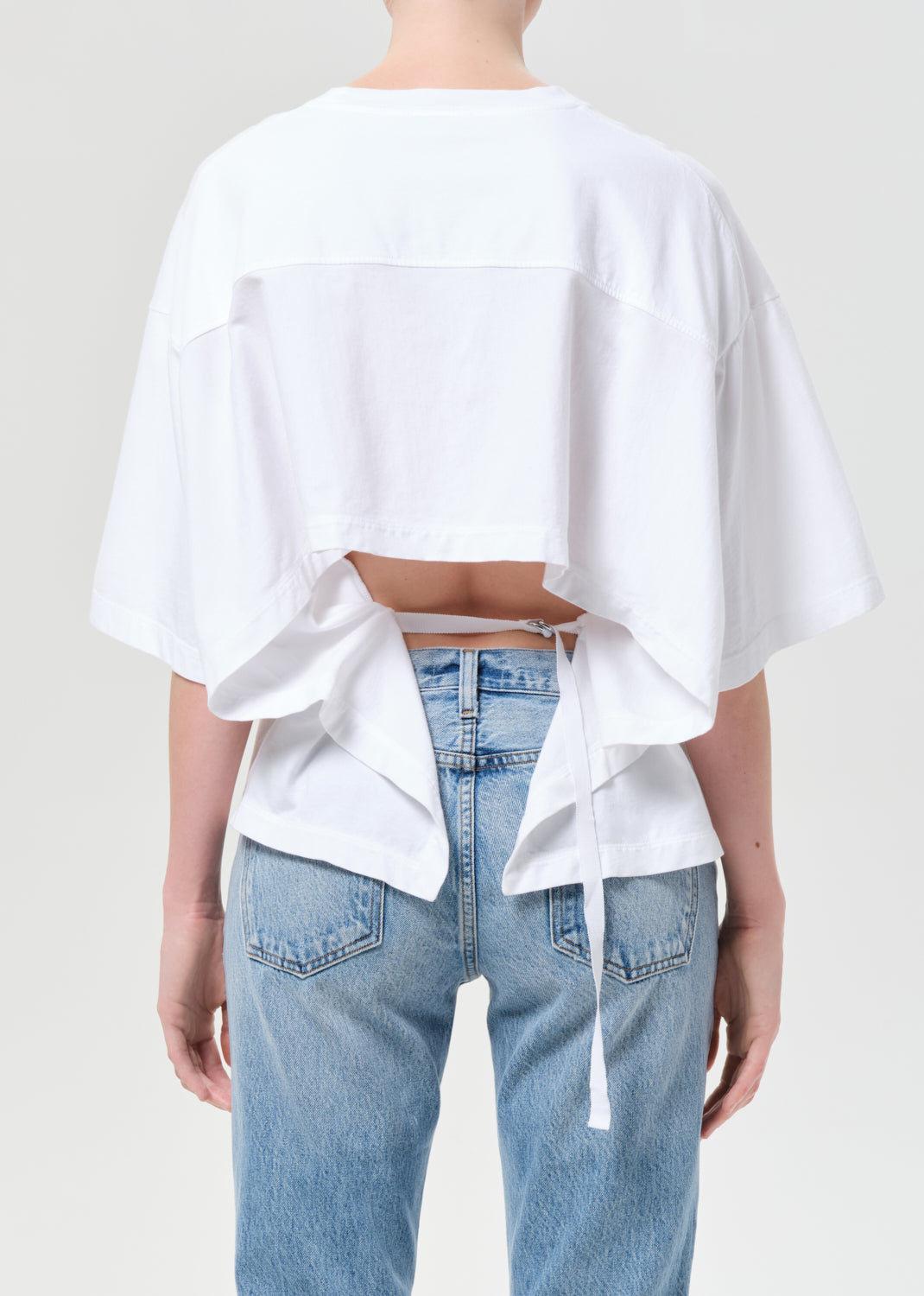 Person wearing a white oversized top and blue jeans on a plain background