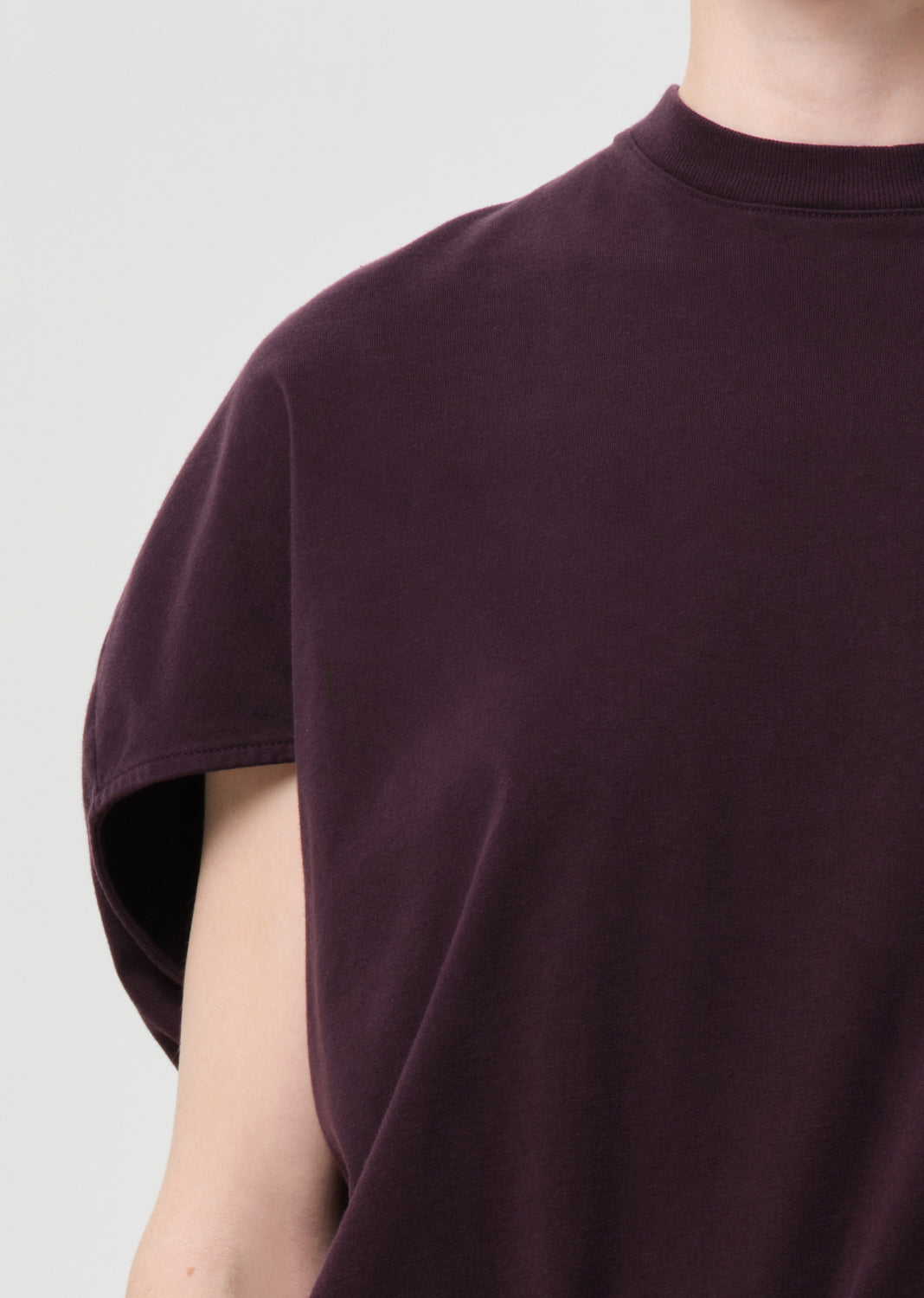 Close-up of a person wearing a dark purple t-shirt against a light gray background