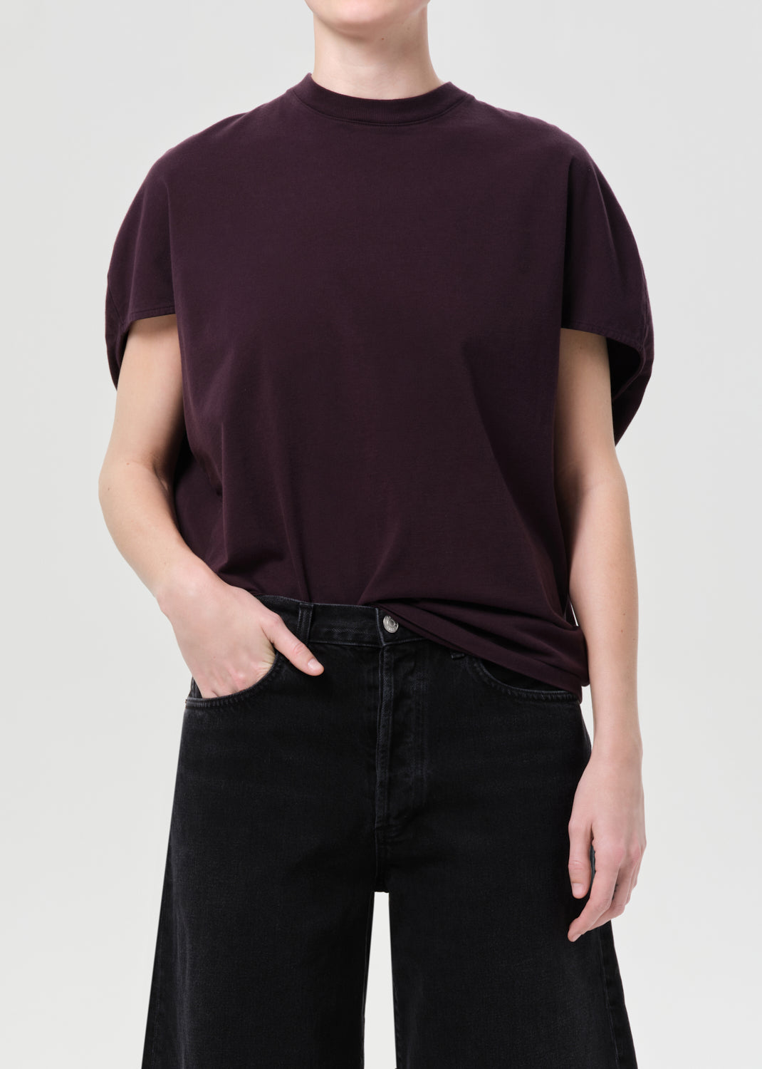 Person wearing a dark purple t-shirt and black pants on a light gray background