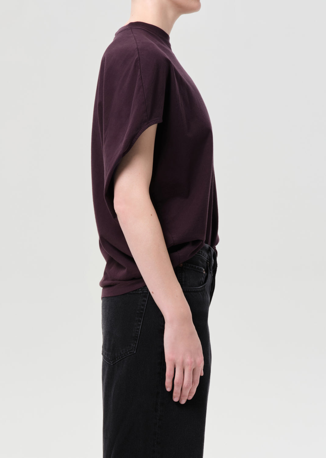 Person wearing a dark purple t-shirt and black pants on a light gray background