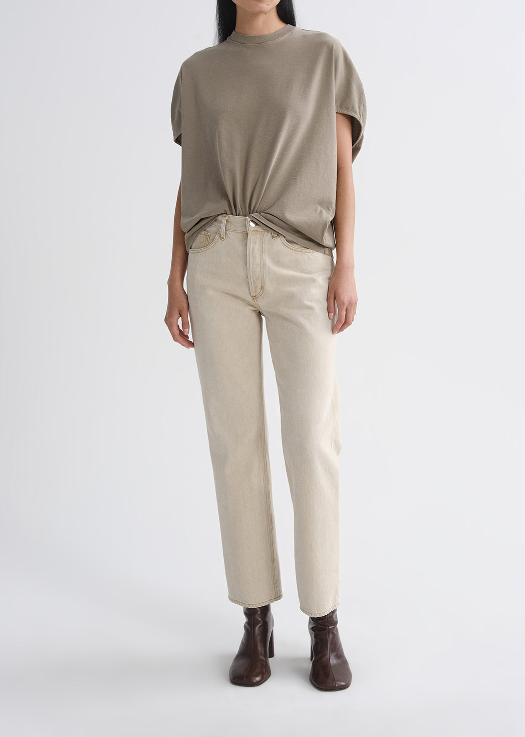 Person wearing a beige top and pants with brown shoes on a grey background