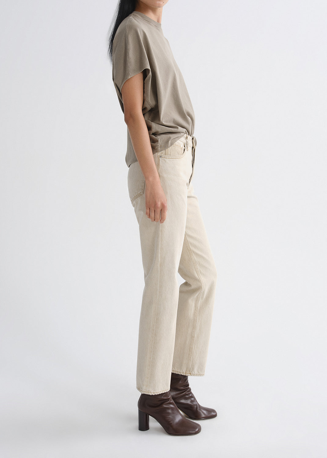 Person wearing a beige top and white pants with brown boots on a grey background
