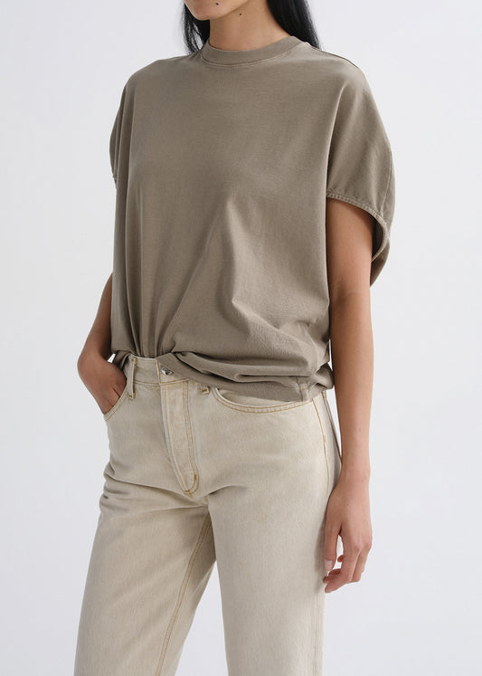 Person wearing a loose-fitting beige t-shirt and light-colored pants on a grey background