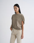 A model wearing a short-sleeve, crew-neck t-shirt in a muted taupe-brown color, paired with light beige jeans, against a plain light gray studio background.