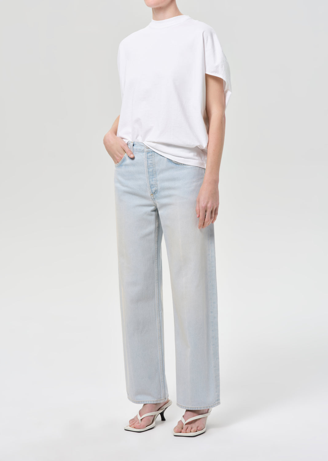 Person wearing light blue jeans and a white t-shirt on a white background