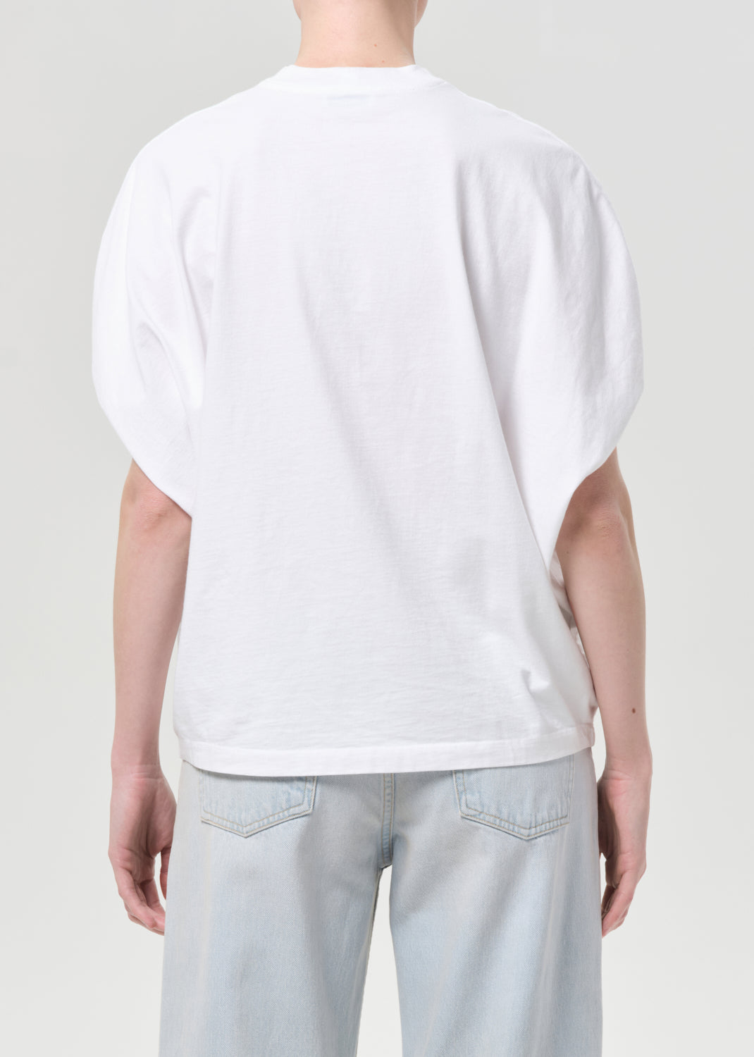 Person wearing a white t-shirt and light blue jeans on a plain background