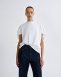 A model wearing a white short-sleeve crewneck t-shirt tucked into dark blue jeans, standing against a light gray studio background.