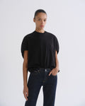 A model wearing a black short-sleeve crewneck t-shirt and dark blue jeans, standing against a light gray studio background.
