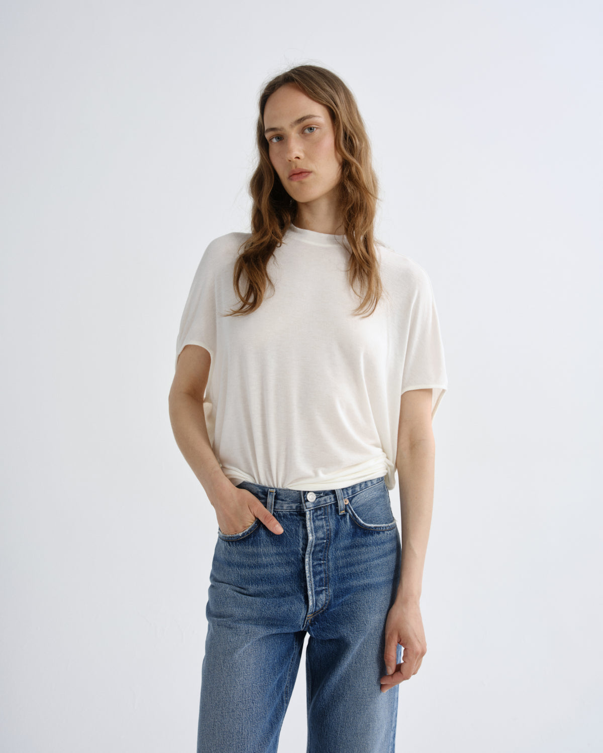 Woman wearing a white t-shirt and blue jeans on a plain background