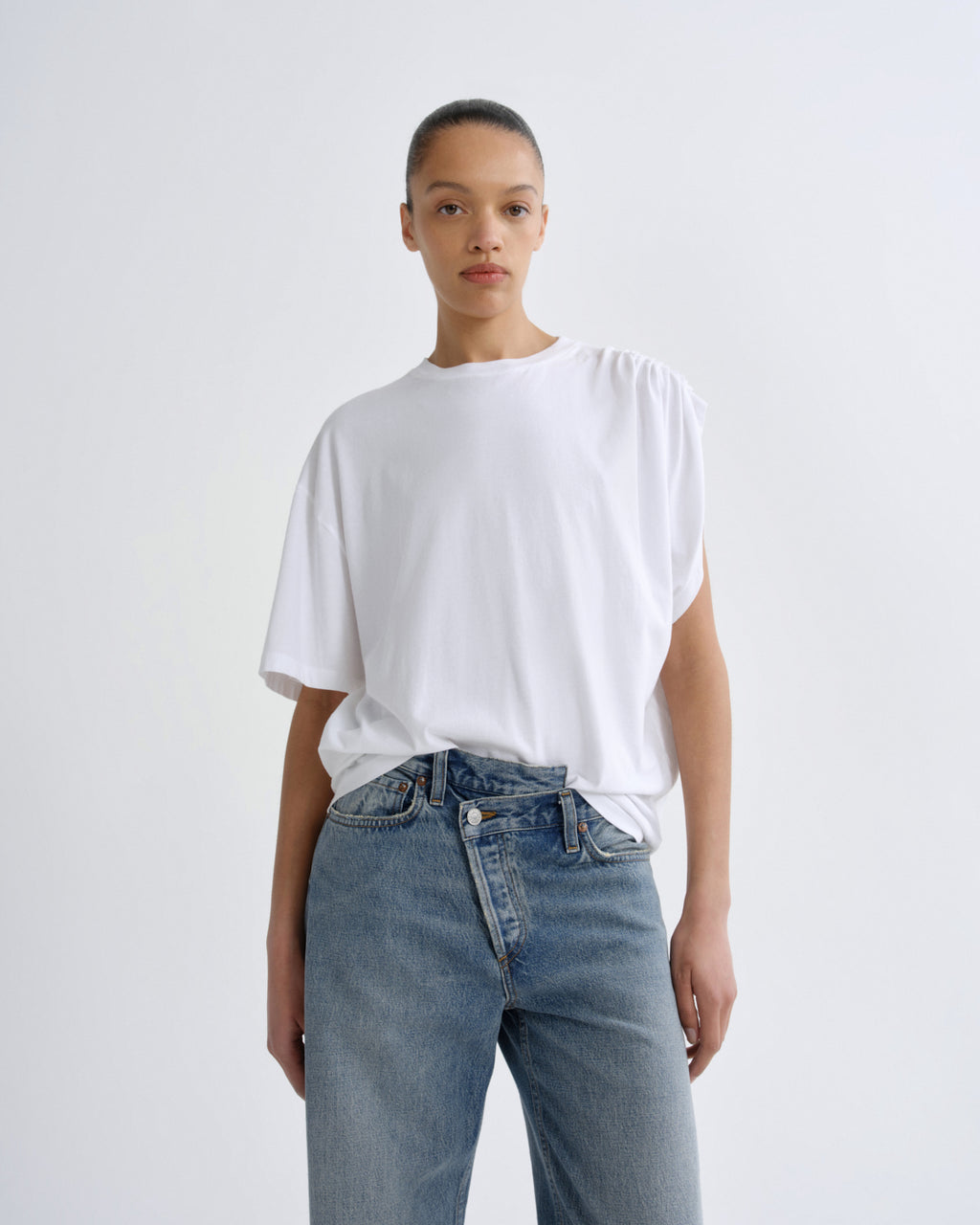 Person wearing a white t-shirt and blue jeans on a plain background