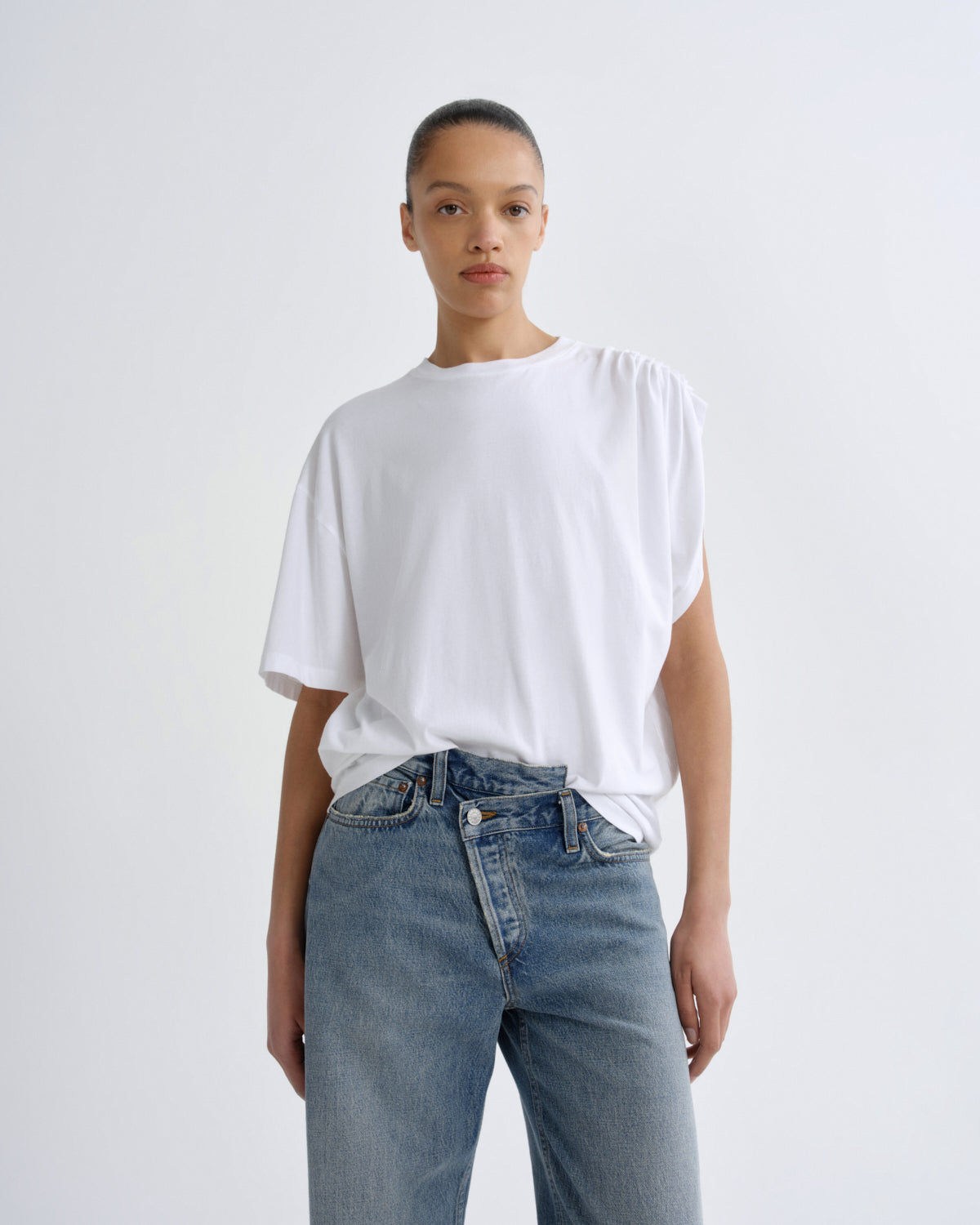 Person wearing a white t-shirt and blue jeans on a plain background
