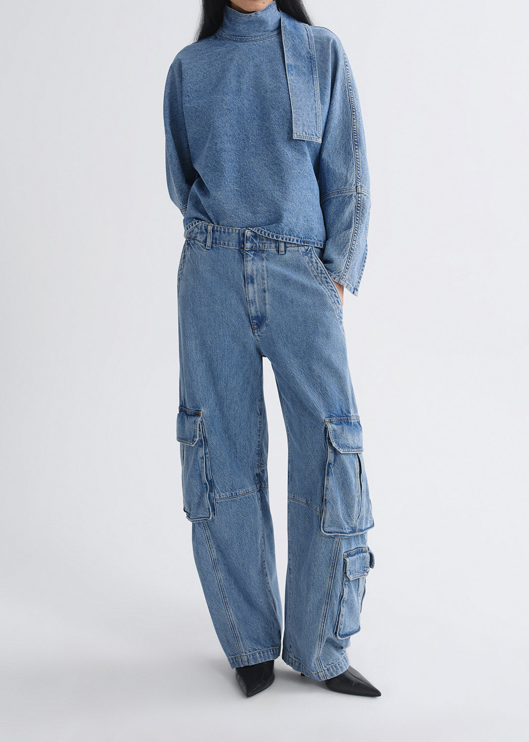 Person wearing a blue denim top and pant on a grey background