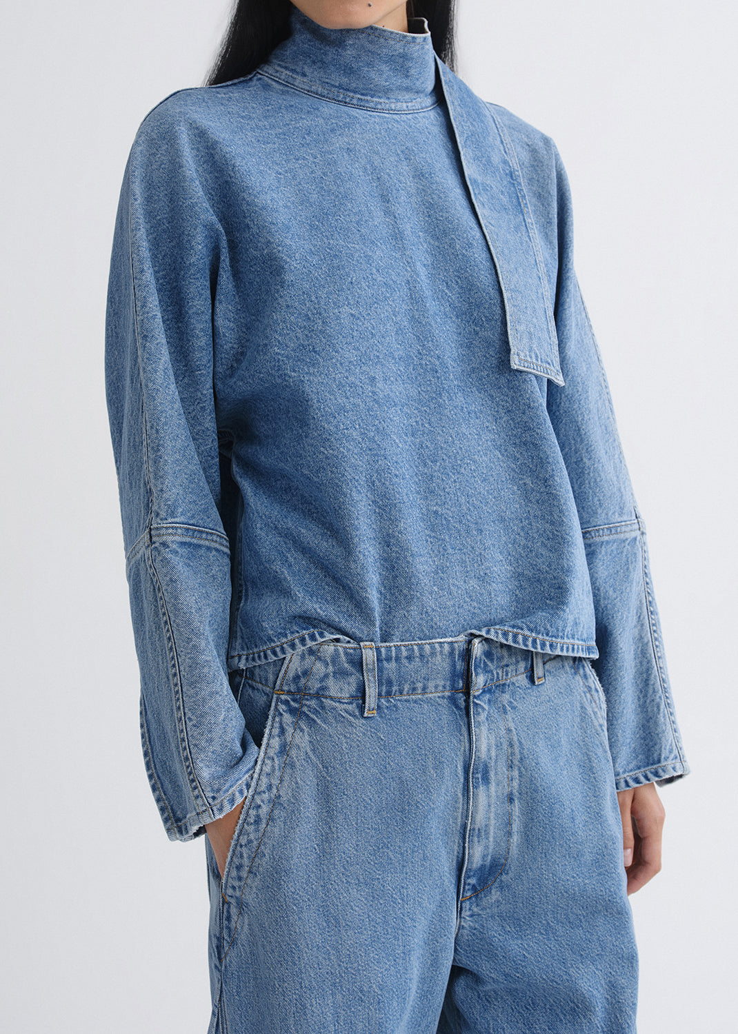 Person wearing a blue denim outfit on a grey background