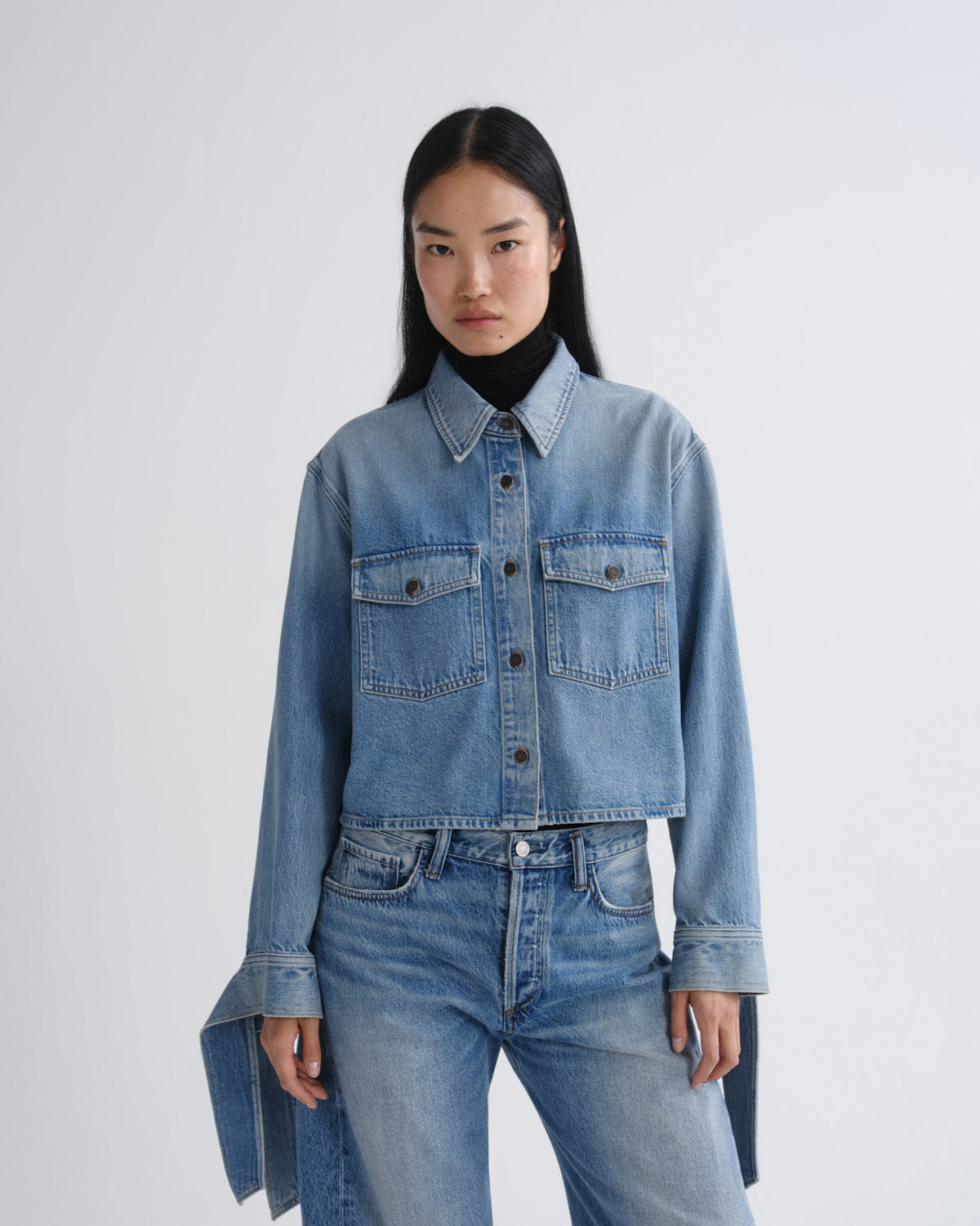 Person wearing a blue denim jacket and jeans on a white background