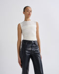 A model wearing a white sleeveless mesh and ruched top paired with black leather pants, standing against a light gray studio background.