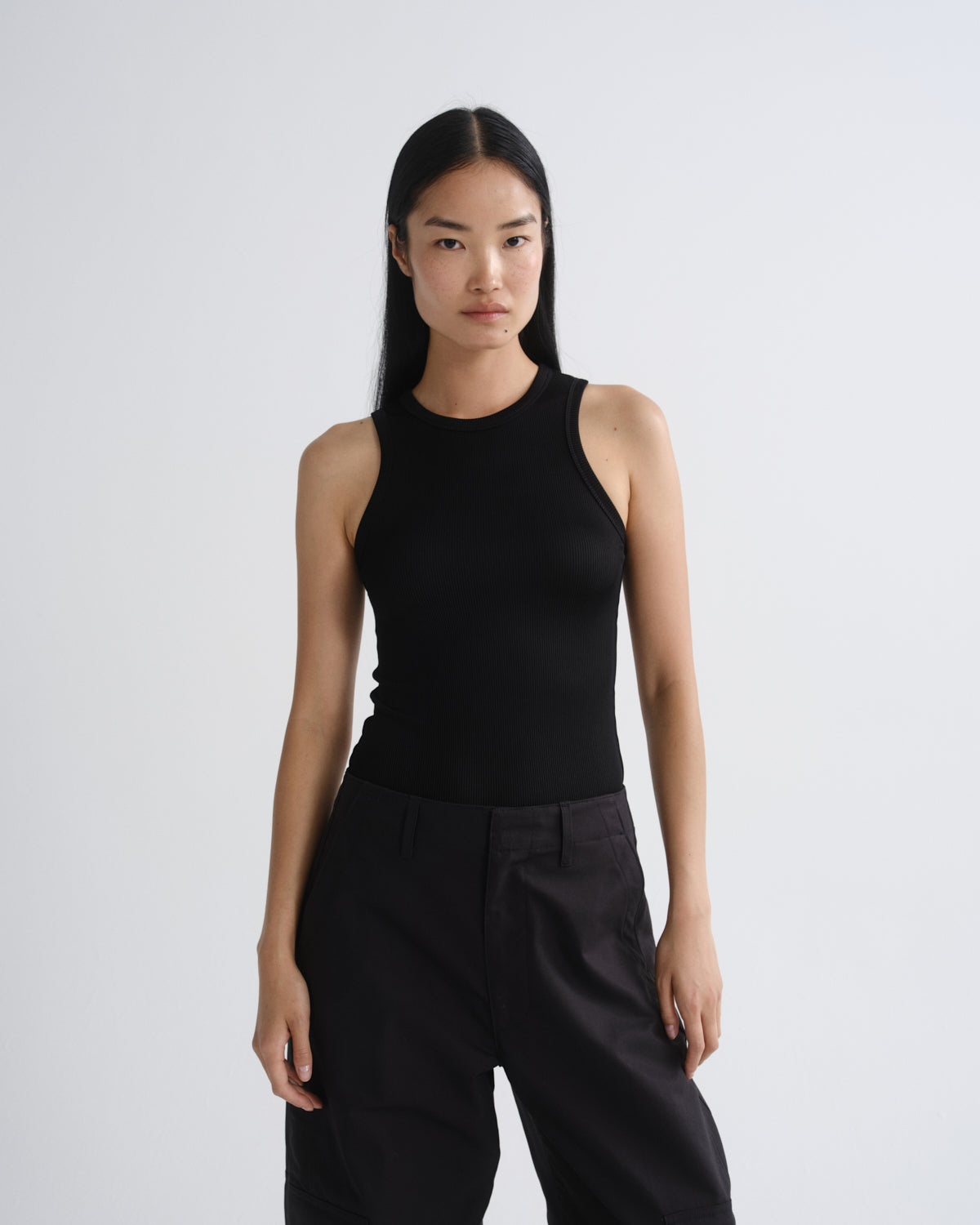 Person wearing a black sleeveless top and black pants on a white background