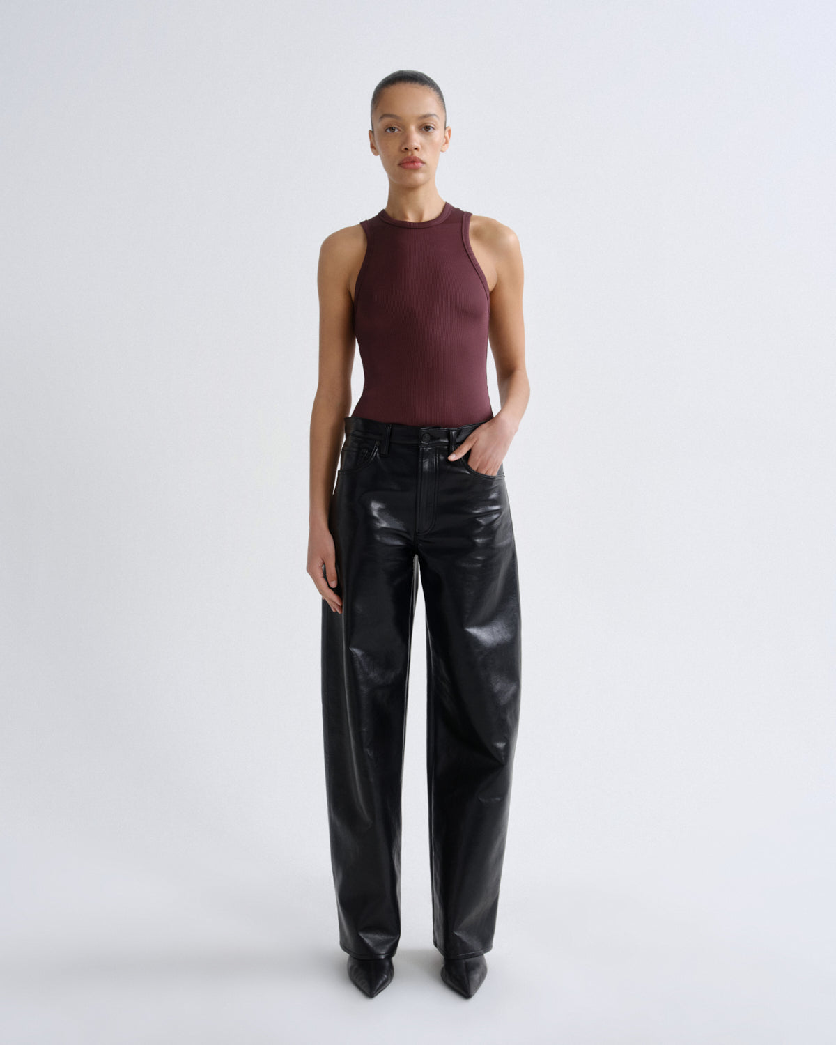 Person wearing a burgundy sleeveless top and black leather pants on a white background