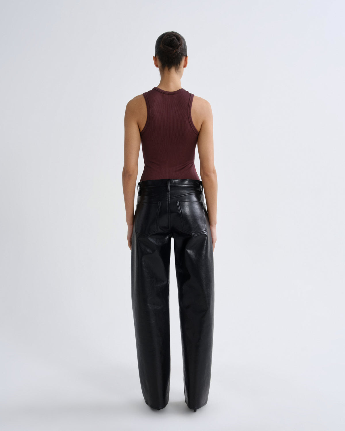 Person wearing a burgundy sleeveless top and black leather pants on a white background