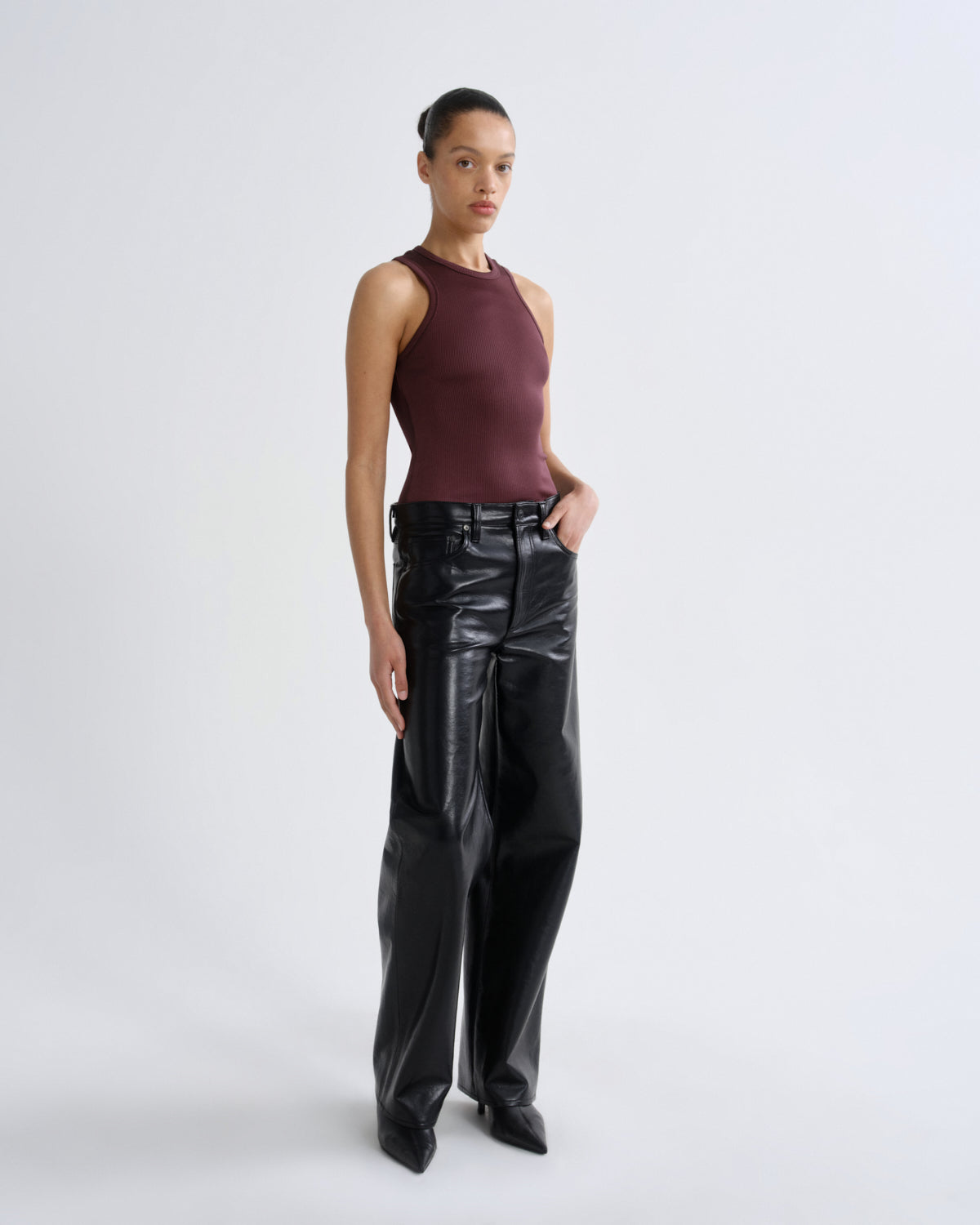 Person wearing a burgundy sleeveless top and black leather pants on a white background