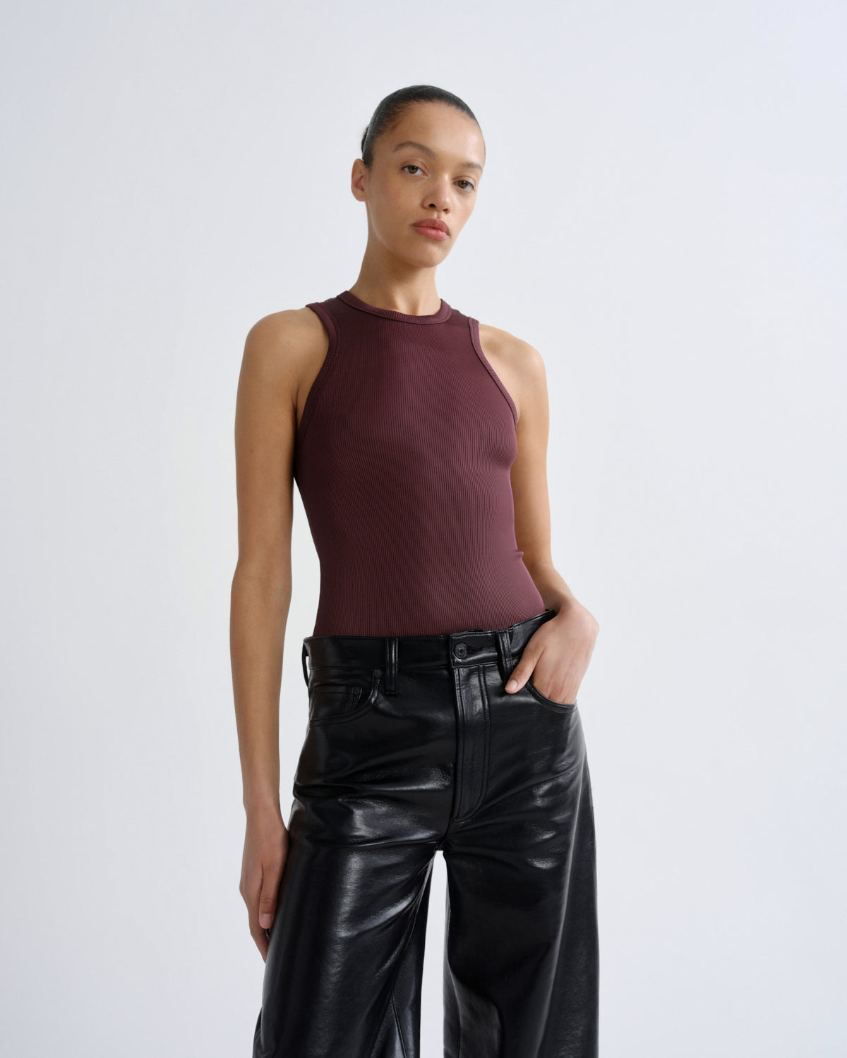 Woman wearing a burgundy sleeveless top and black leather pants on a white background