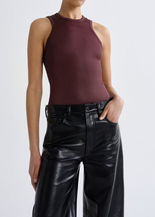A model wearing a sleeveless, high-neck ribbed knit top in a deep burgundy shade, paired with black wide-leg faux-leather pants, against a grey background.