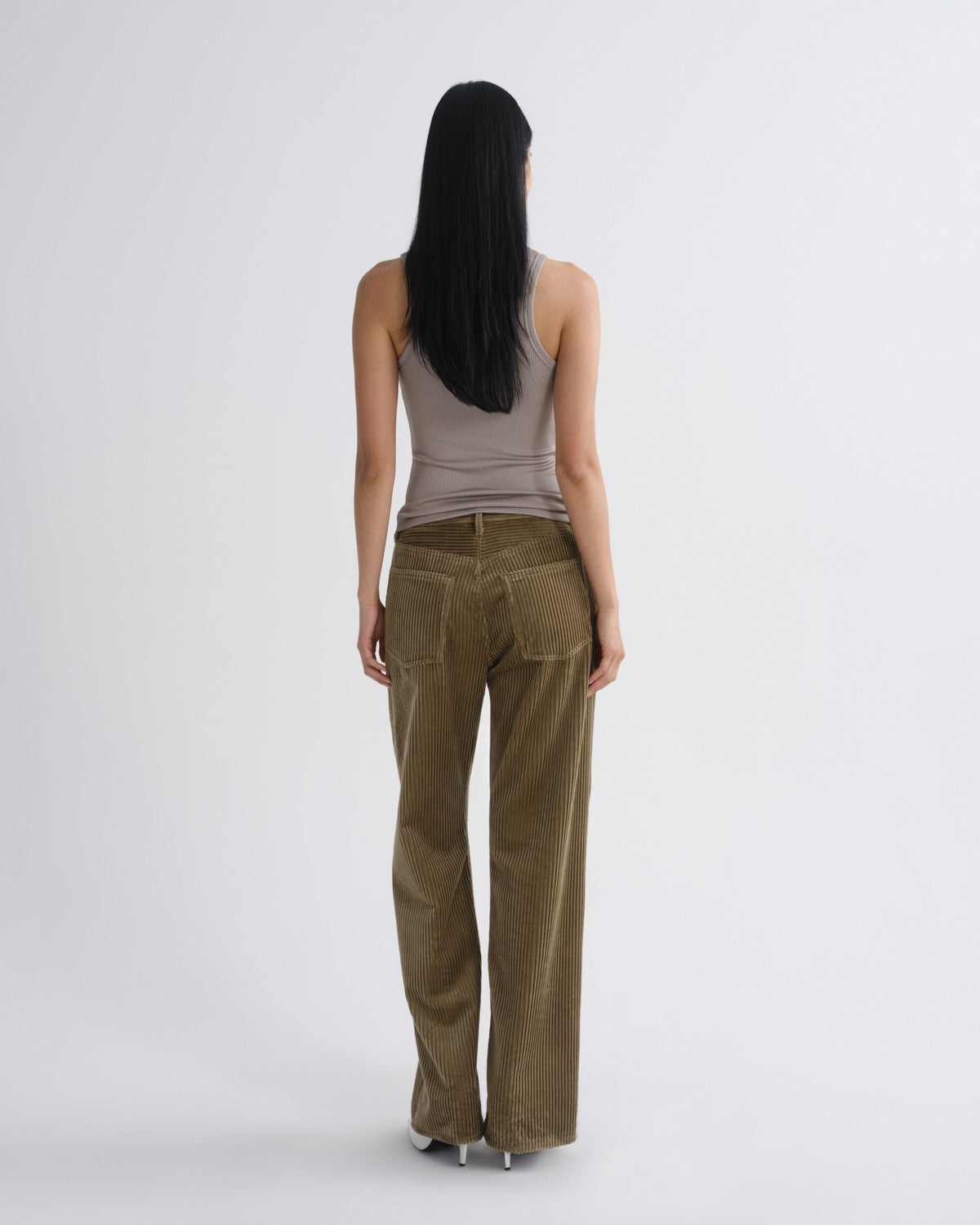 Person wearing brown corduroy pants and a gray tank top on a white background