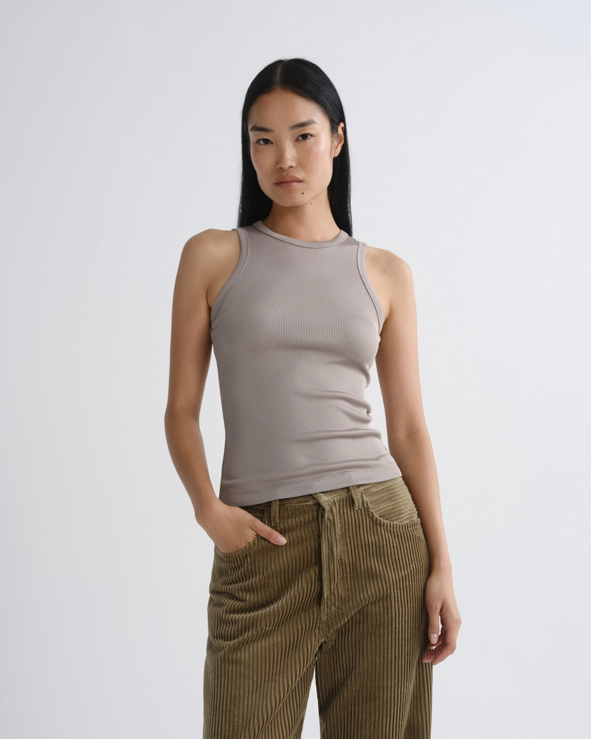 Woman wearing a beige tank top and brown corduroy pants on a white background