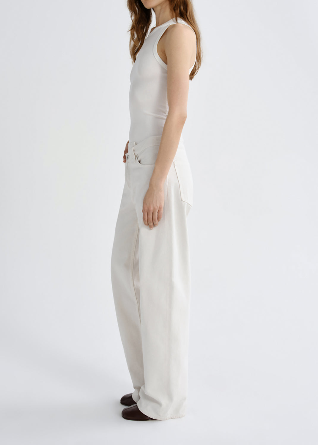 A model shown from the side wearing a sleeveless white top and matching wide-leg trousers, photographed against a grey background.