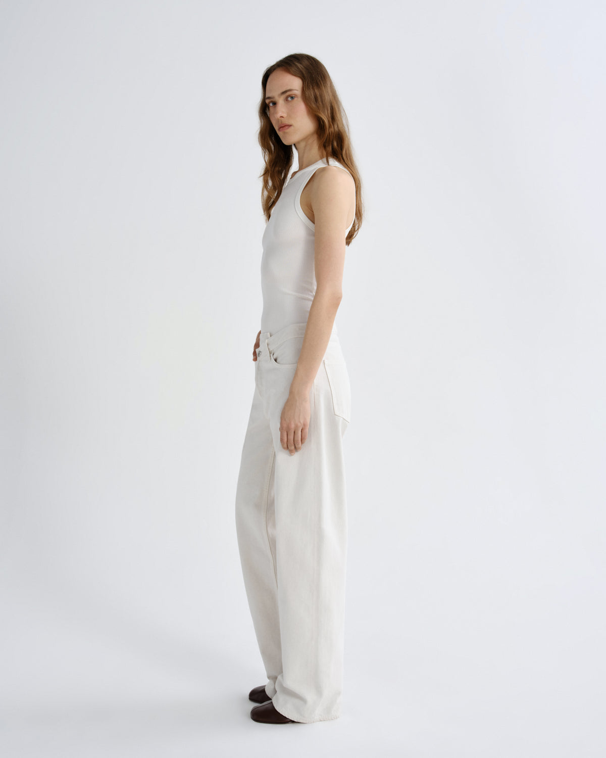 Woman wearing a white sleeveless top and pants on a light gray background