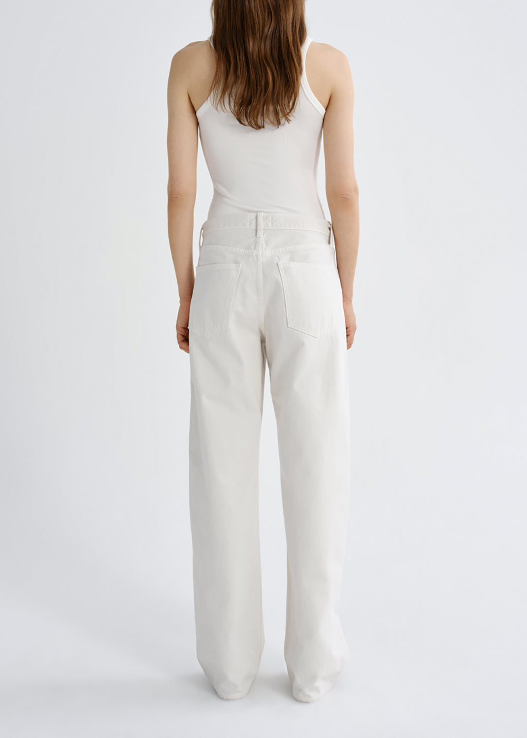 A model shown from the back wearing a white ribbed camisole top and matching white wide-leg trousers against a grey background.