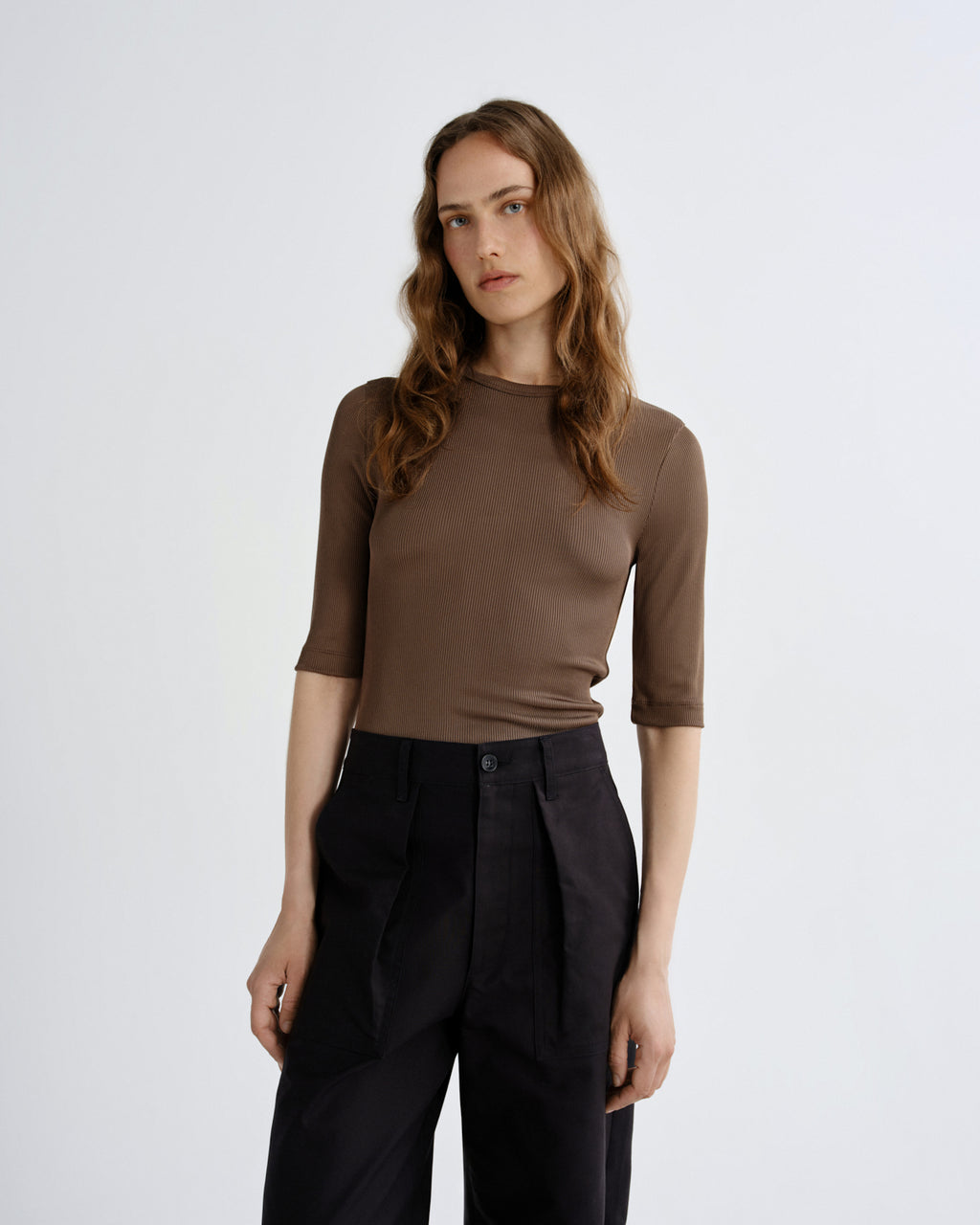 Woman wearing a brown top and black pants on a white background