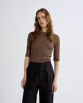 Woman wearing a brown top and black pants on a white background