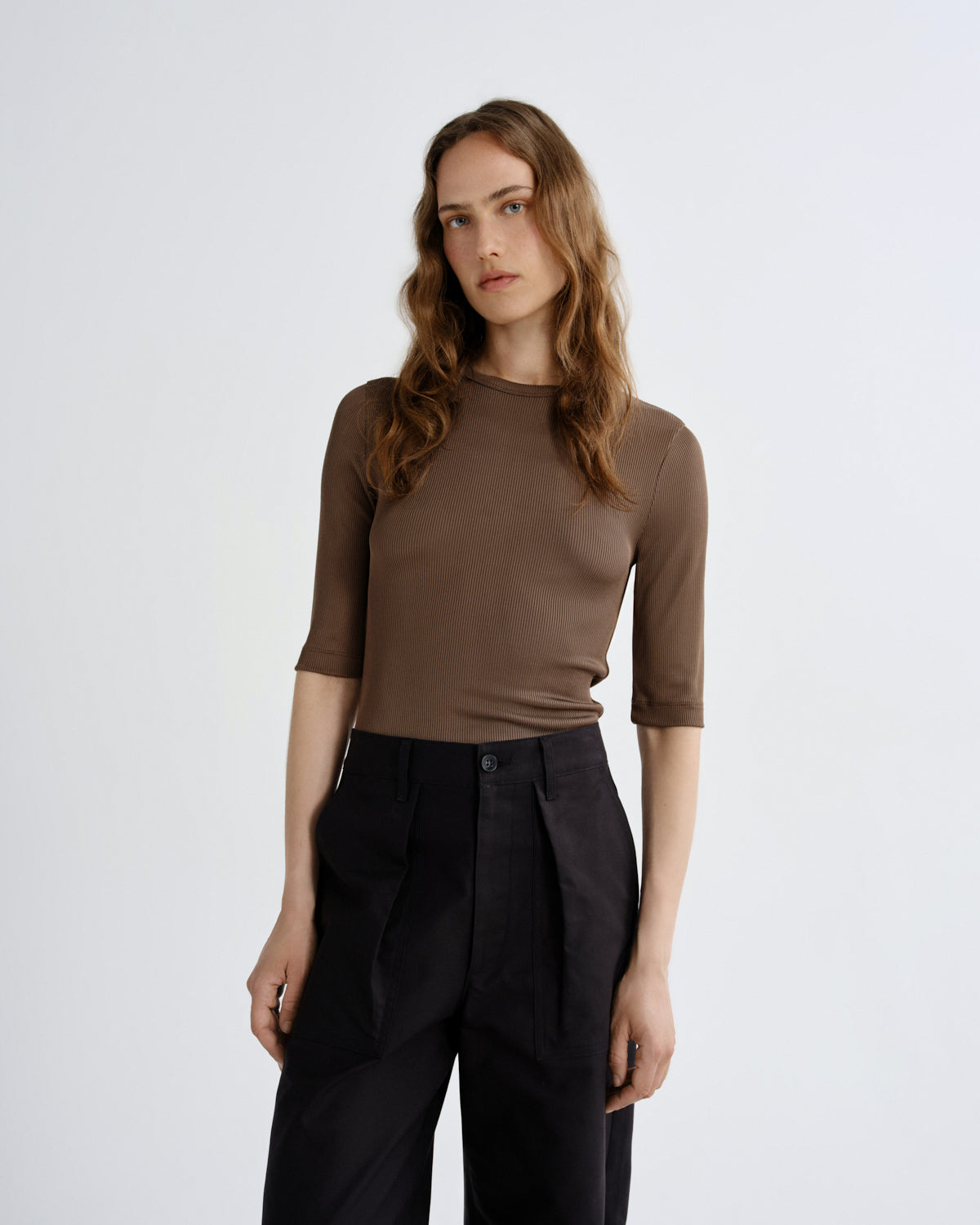 Woman wearing a brown top and black pants on a white background