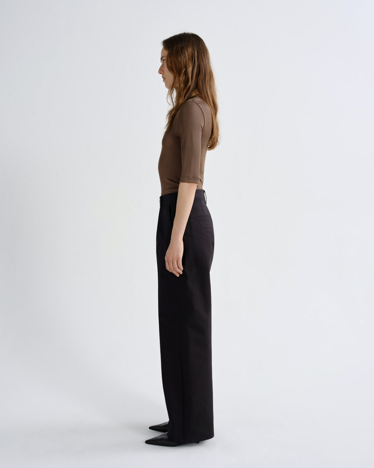Woman wearing a brown top and black pants on a white background