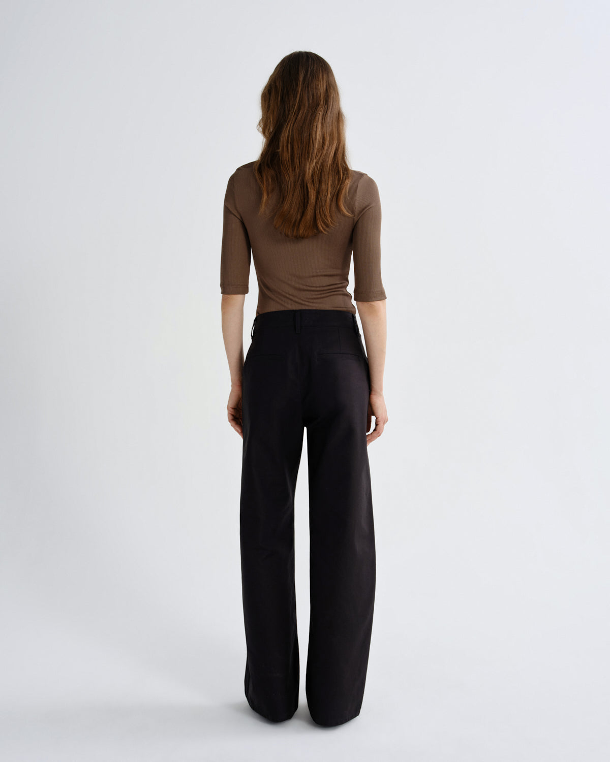Woman wearing a brown top and black pants on a white background