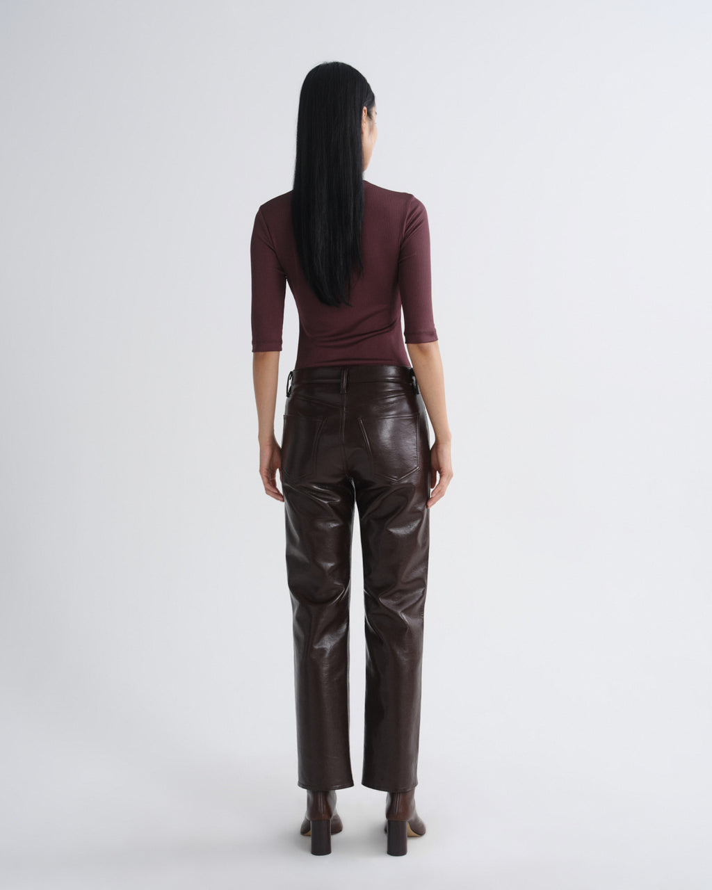 Person wearing a burgundy top and brown leather pants on a white background