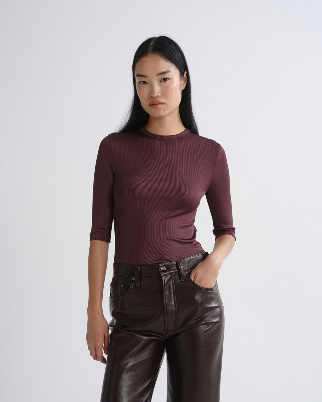 Woman wearing a maroon long-sleeve top and brown leather pants on a white background