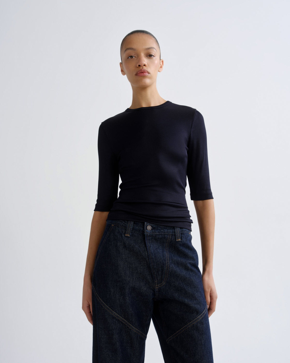 Person wearing a black top and dark jeans on a white background