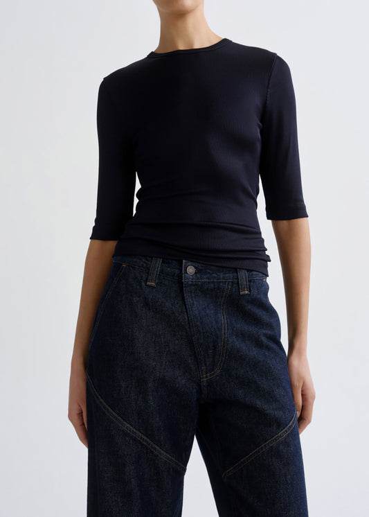 A model wearing a dark navy blue 3/4-sleeve crewneck top and dark blue denim jeans, shown from the neck down against a grey background.