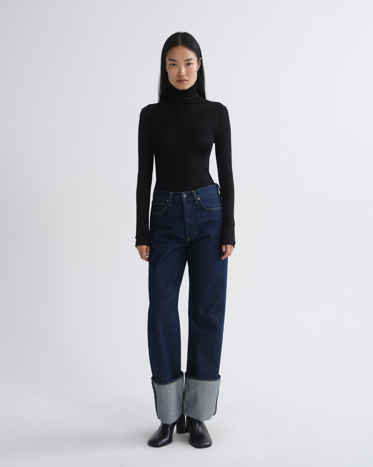 Person wearing a black turtleneck and blue jeans on a white background