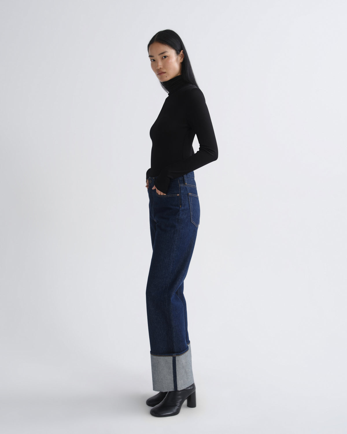 Person wearing a black turtleneck and dark blue jeans on a white background