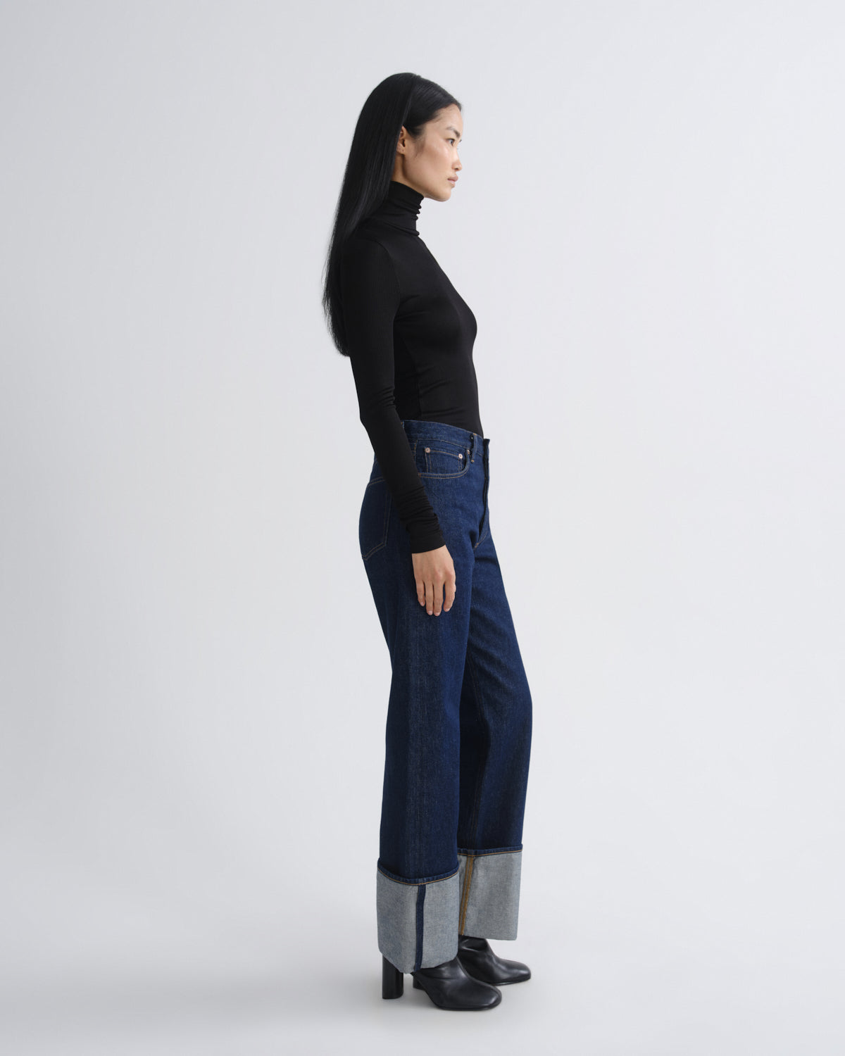 Person wearing dark blue jeans with a black top on a white background