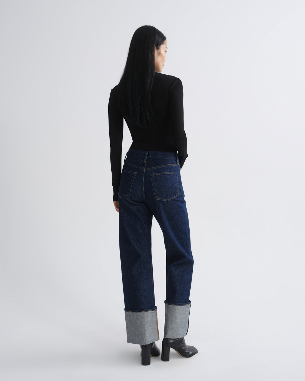 Person wearing dark blue jeans with gray cuffs on a white background