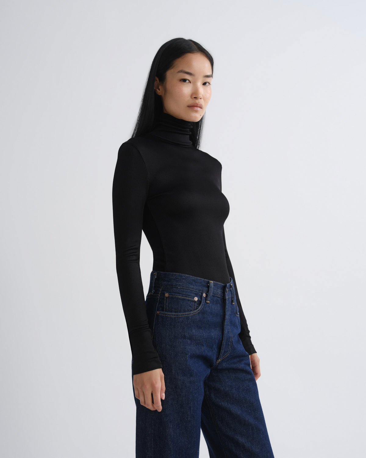 Person wearing a black turtleneck and blue jeans on a white background