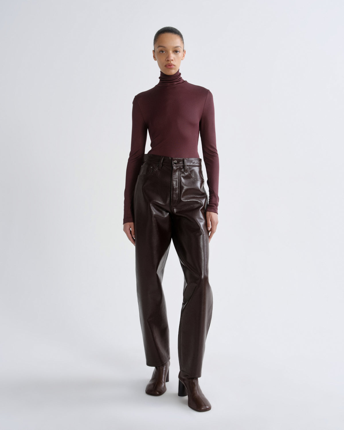 Person wearing a burgundy turtleneck and shiny brown pants on a white background