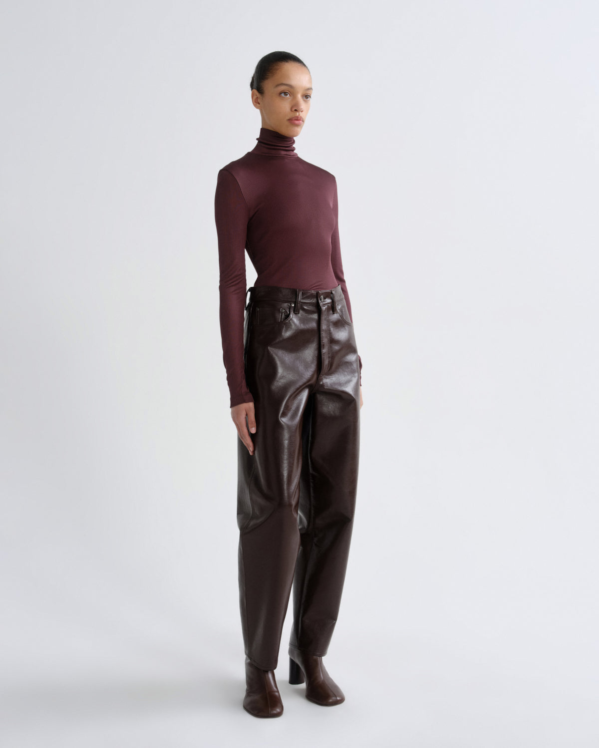 Person wearing a burgundy turtleneck and dark brown leather pants on a white background
